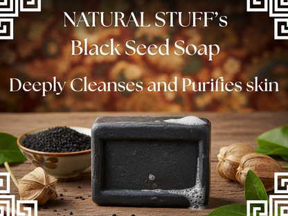 Black seed soap with a bowl of black seeds on a wooden surface, surrounded by leaves.