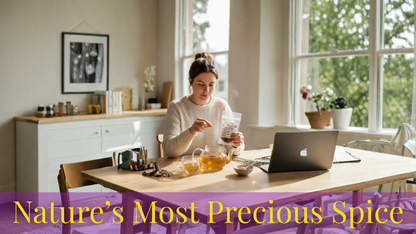 Woman sitting at a table with a laptop and a glass of tea, surrounded by plants and decor.